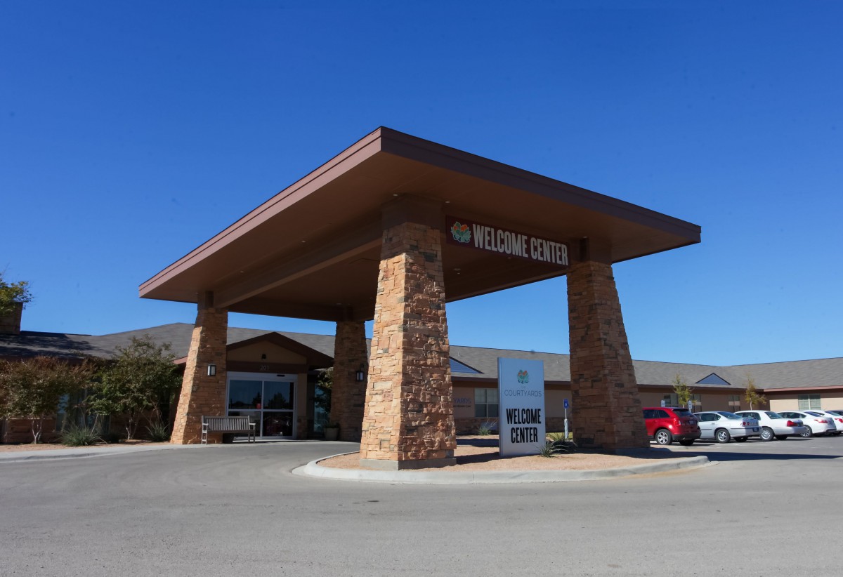 A roadside motel with a stone entrance and parking area under a clear blue sky.