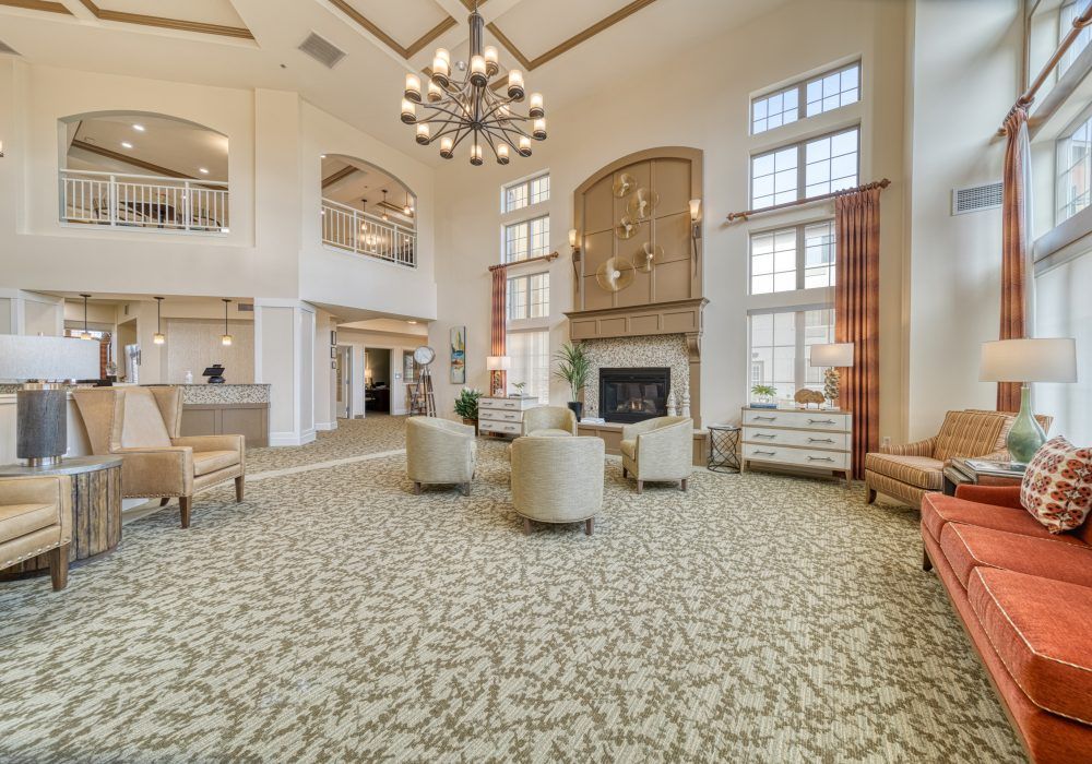 A spacious and elegant living room featuring a grand chandelier, comfortable seating area, and a fireplace with high ceilings.
