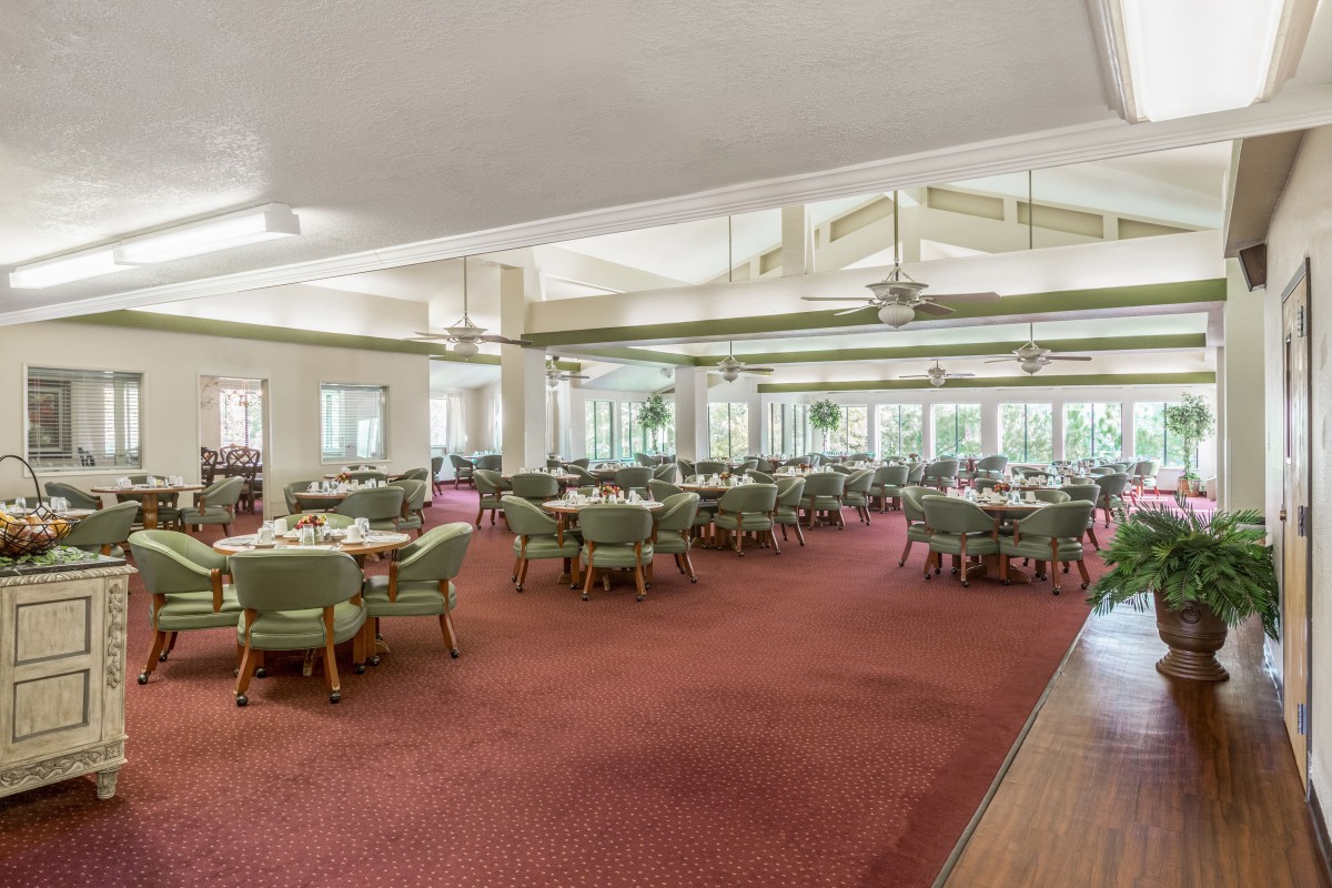 An empty dining room with neatly arranged tables and chairs, featuring large windows and a carpeted floor.