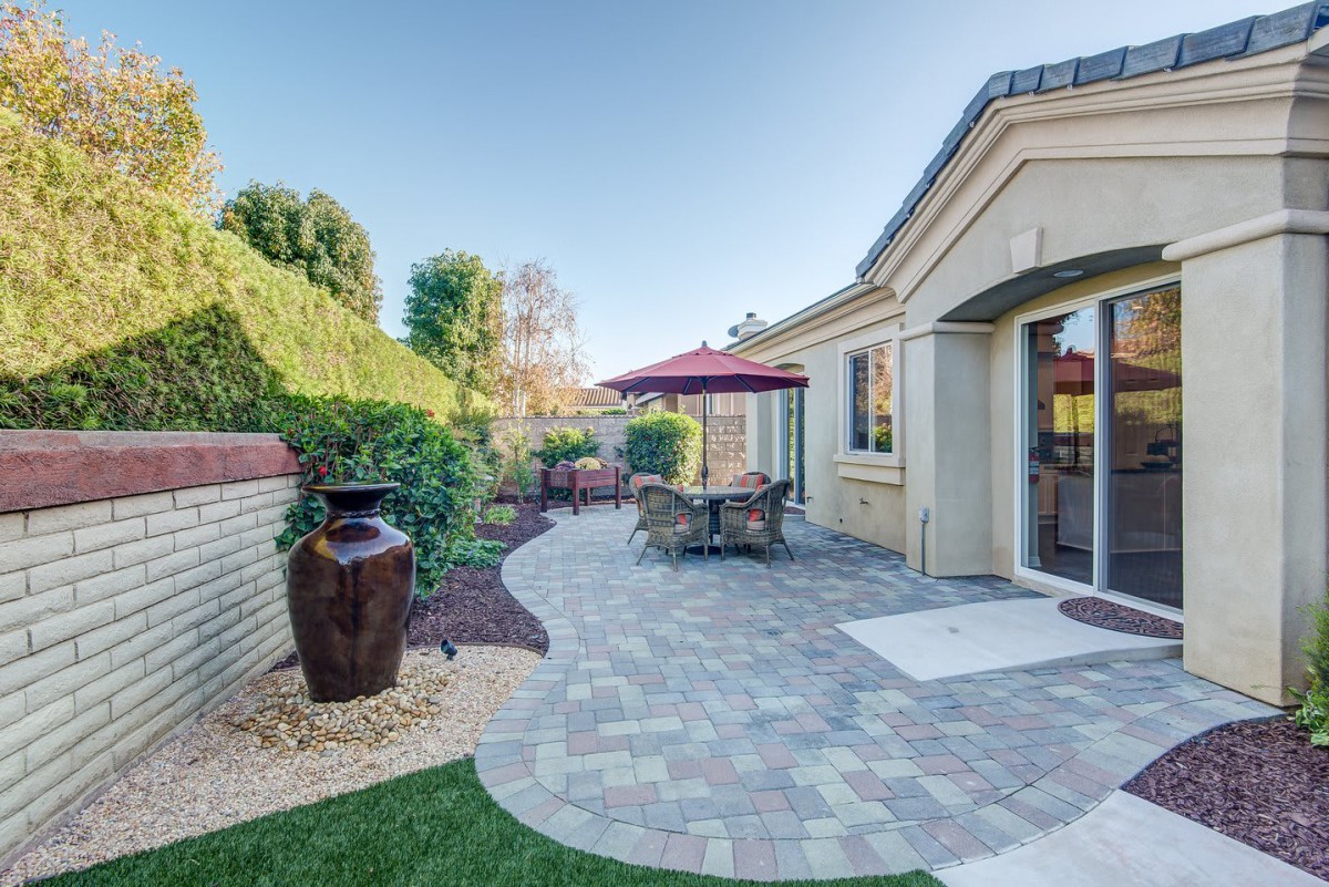 A beautifully landscaped backyard patio with an outdoor dining area and large decorative pot, under a sunny sky.
