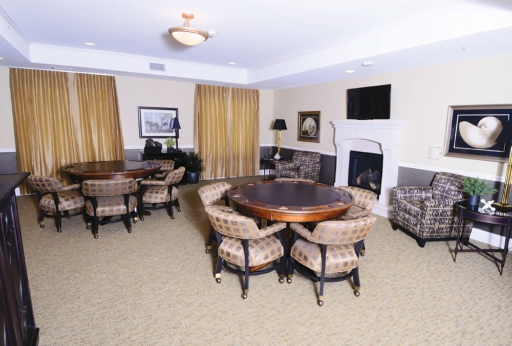A cozy living room featuring seating areas with round tables, upholstered chairs, a fireplace, and a wall-mounted television.