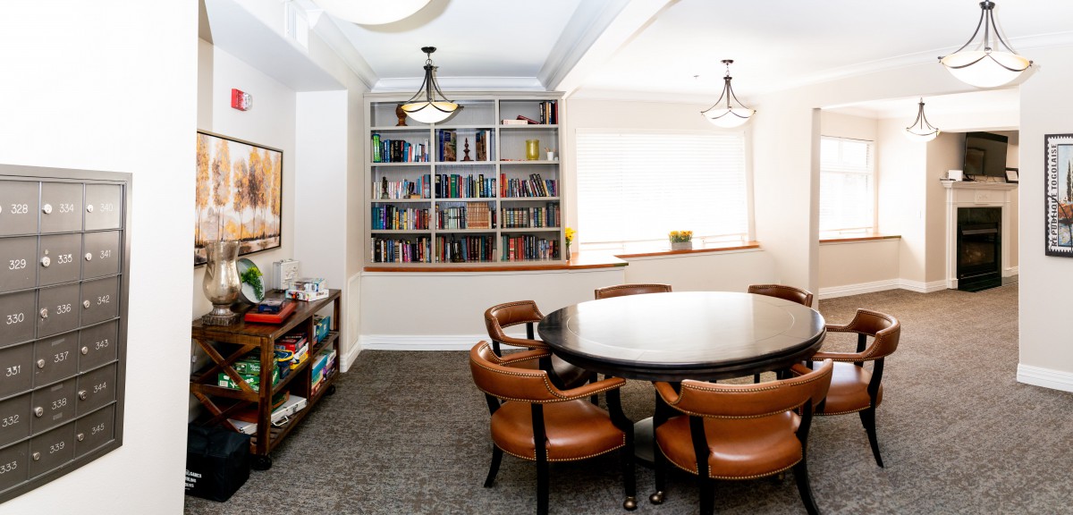A cozy library corner featuring a round table with leather chairs and a well-stocked bookshelf.