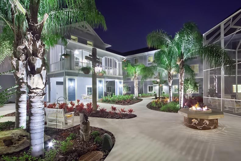 A beautiful modern house illuminated at night, surrounded by palm trees and landscaped gardens.