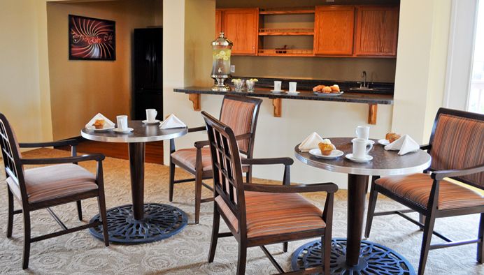 A cozy dining area featuring tables and chairs set with coffee cups, near a breakfast bar.