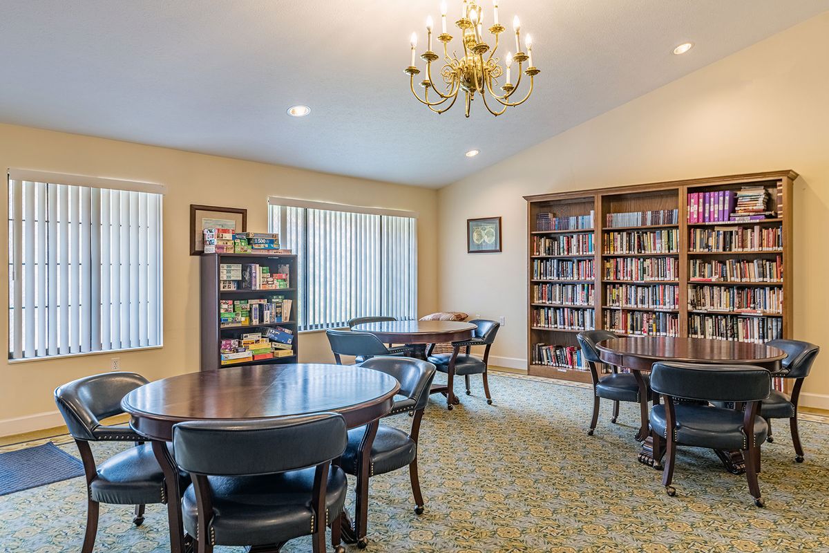 A cozy reading room with bookshelves, tables, and a chandelier.