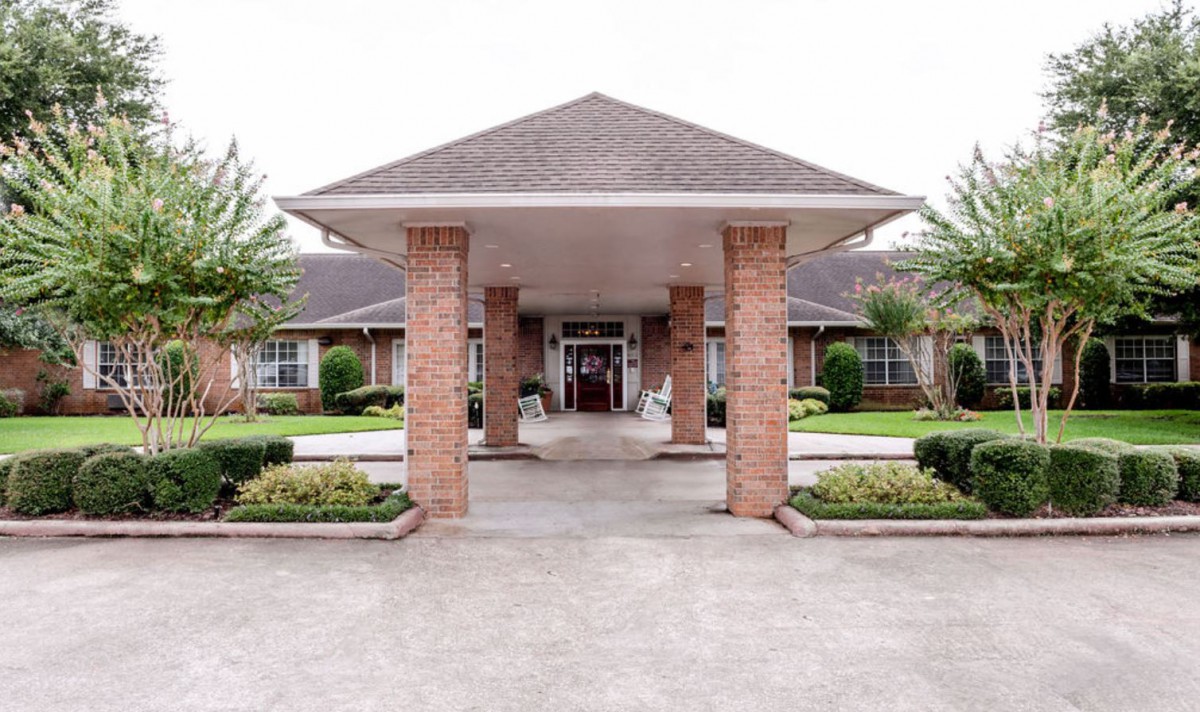A building entrance with brick pillars and a covered walkway, surrounded by well-maintained landscaping.