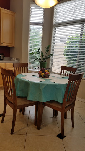 A cozy dining area featuring a round table with a turquoise tablecloth and a centerpiece of fruits, complemented by the warmth of natural light.