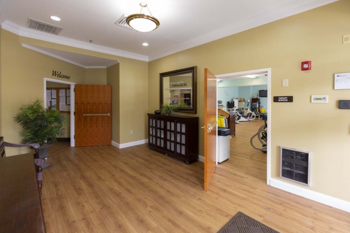 A welcoming lobby area with wood flooring, a mirror on the wall, and an open door leading to another room.