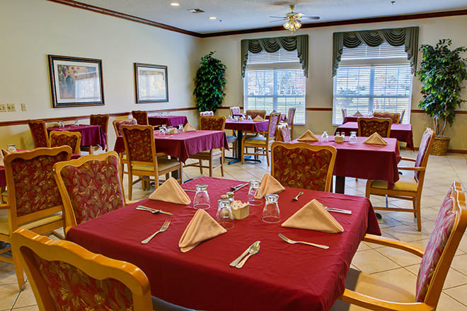 A neatly arranged dining area with tables set for a meal, featuring red tablecloths and cloth napkins.
