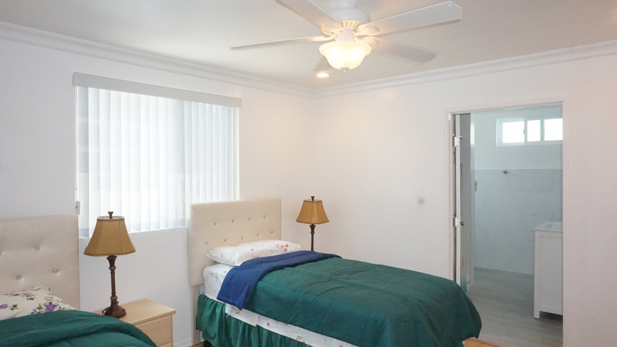 A simple bedroom featuring a single bed with green bedding, a bedside lamp, and a ceiling fan.
