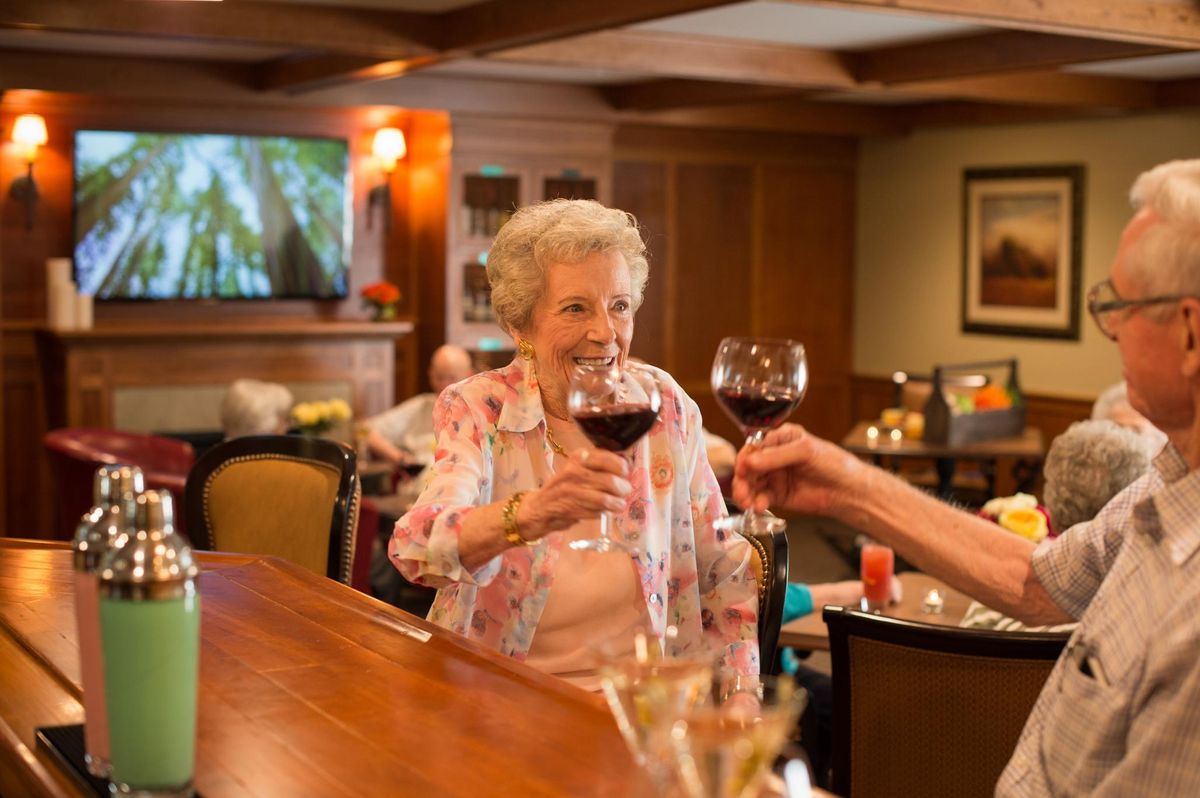 An elderly woman enjoying a glass of wine at a bar, engaging in a cheerful toast.