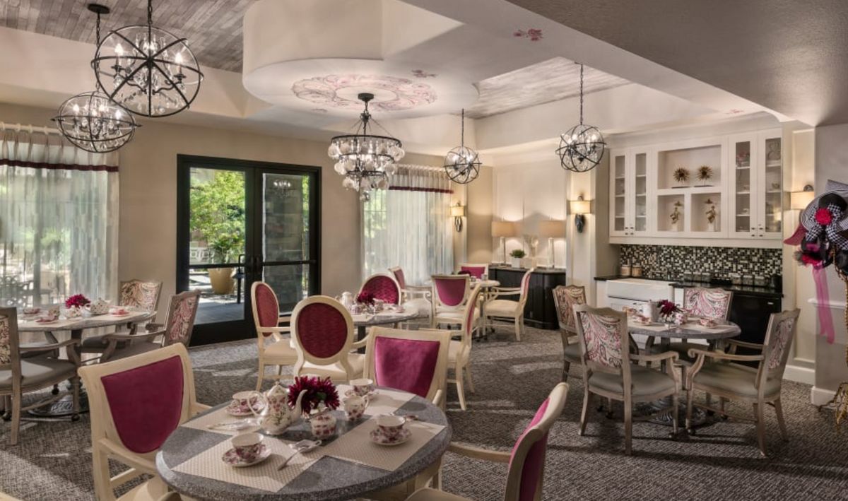 An elegant tea room with luxurious decor, featuring ornate tables and chairs under beautiful chandeliers.