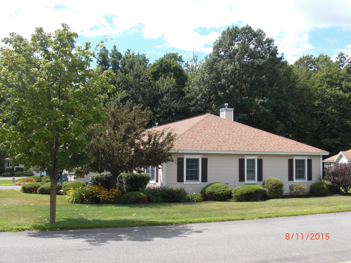 A suburban house with a well-maintained lawn and surrounding trees on a sunny day.