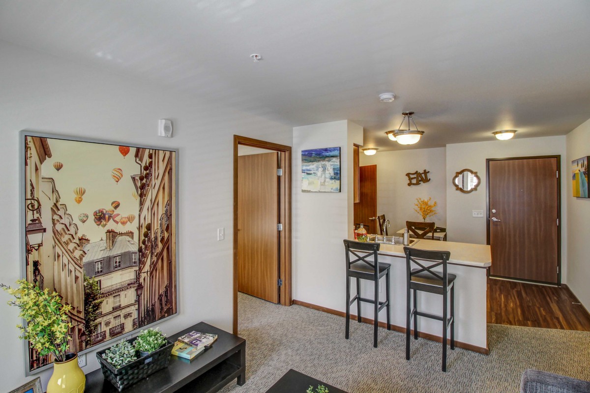 A cozy living room with a view of the kitchen area, featuring bar stools and decorative artwork.