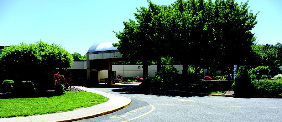 A driveway leading to a building entrance, surrounded by trees on a sunny day.