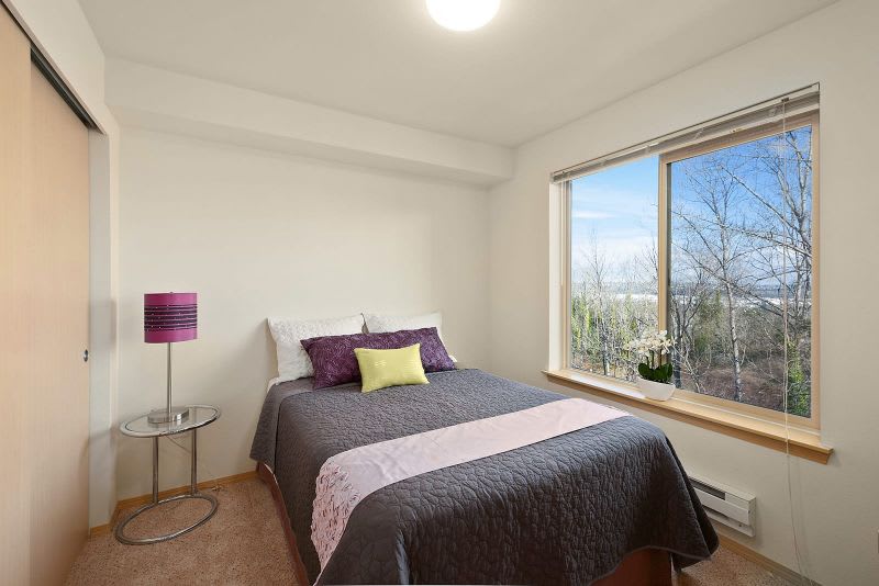 A well-lit minimalist bedroom with a double bed, colorful lamp, and large window.