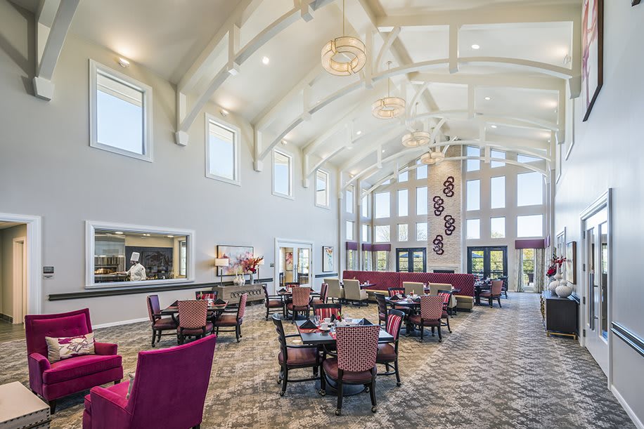 A spacious and elegantly designed dining area with high ceilings and large windows, featuring comfortable seating arrangements.