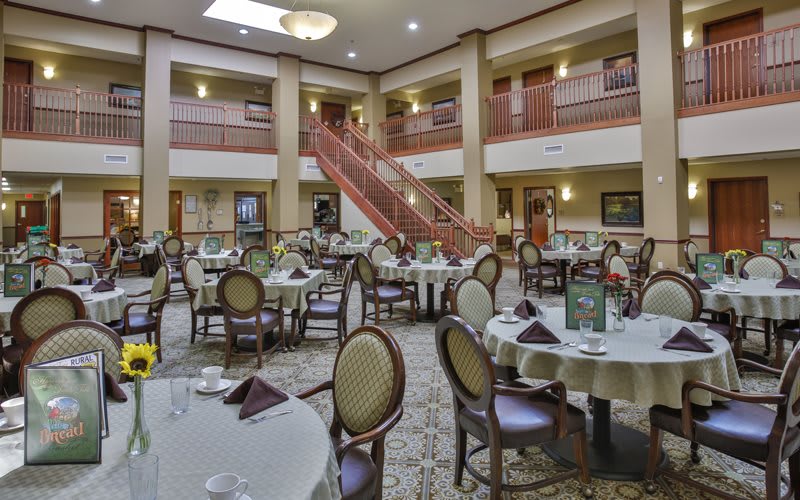 A spacious dining area with elegantly set tables and a grand staircase in the background.