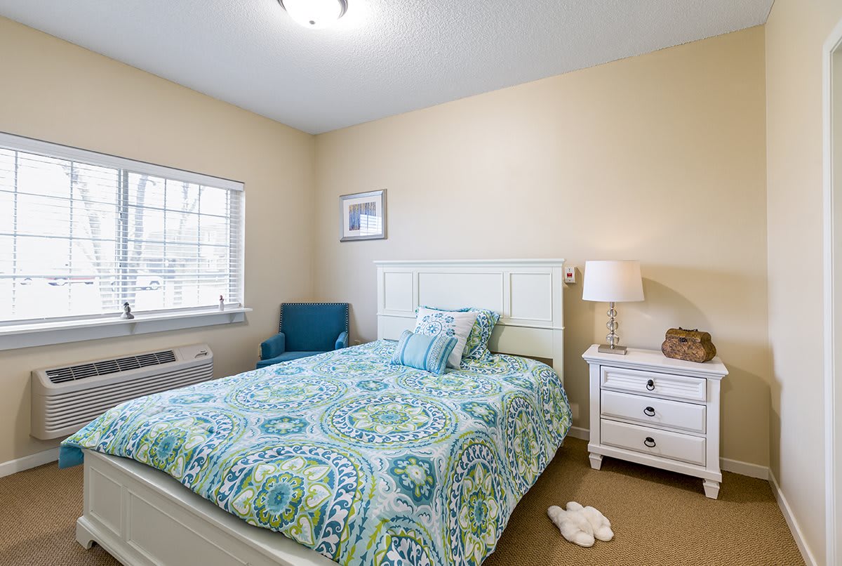 A cozy bedroom with a patterned bedspread, nightstand, and blue armchair.