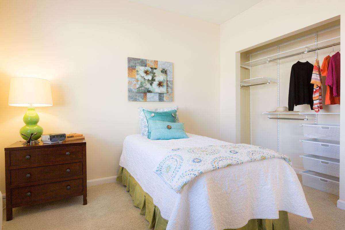 A cozy bedroom with a single bed, decorative pillows, and an open closet.