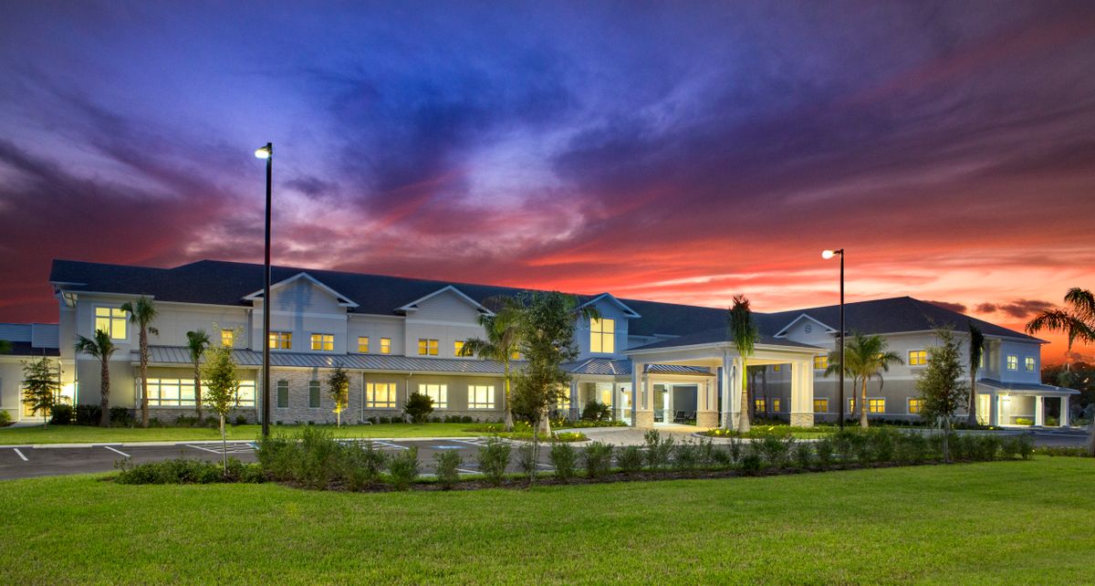 A beautifully lit building sits against a vibrant sunset sky with a well-maintained lawn in the foreground.