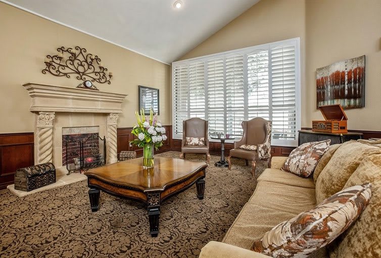 A cozy living room with elegant decor, featuring a plush sofa, wooden coffee table, fireplace, and large windows with shutters.