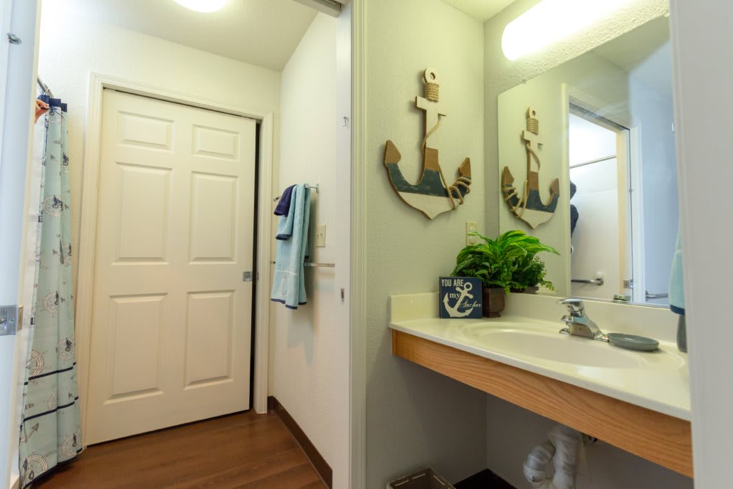 A bathroom featuring a sink with a decorative anchor mirror, potted plant, and towels.