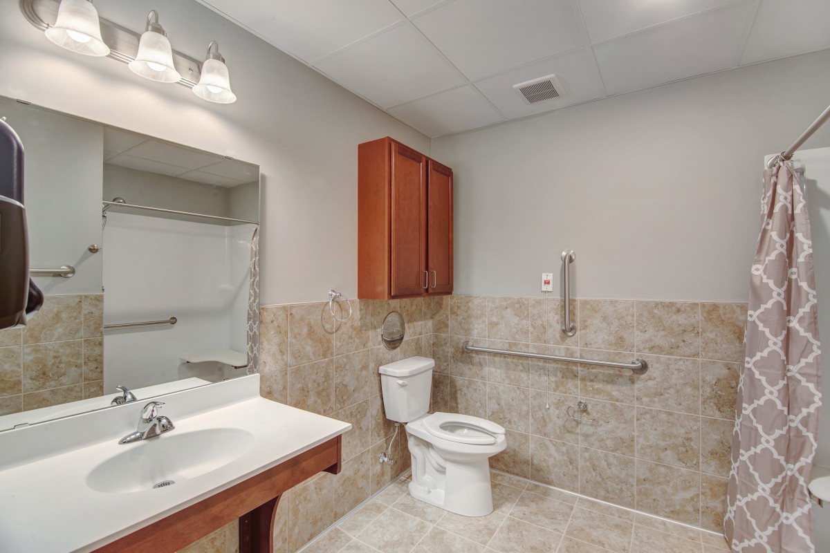 A modern bathroom with a sink, toilet, and wooden cabinet, featuring tiled walls and floor.