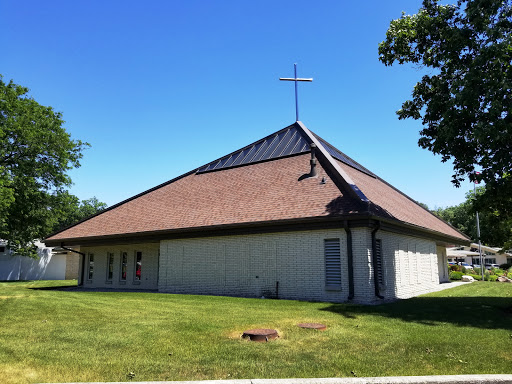 A modern church building with a cross on top, surrounded by green grass.