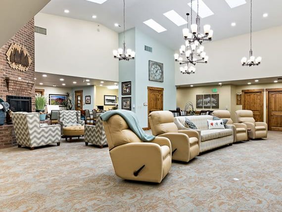 A spacious and modern living room with comfortable recliner chairs, sofas, and elegant chandeliers.