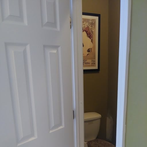 A partially open door reveals a bathroom with a toilet and framed artwork on the wall.