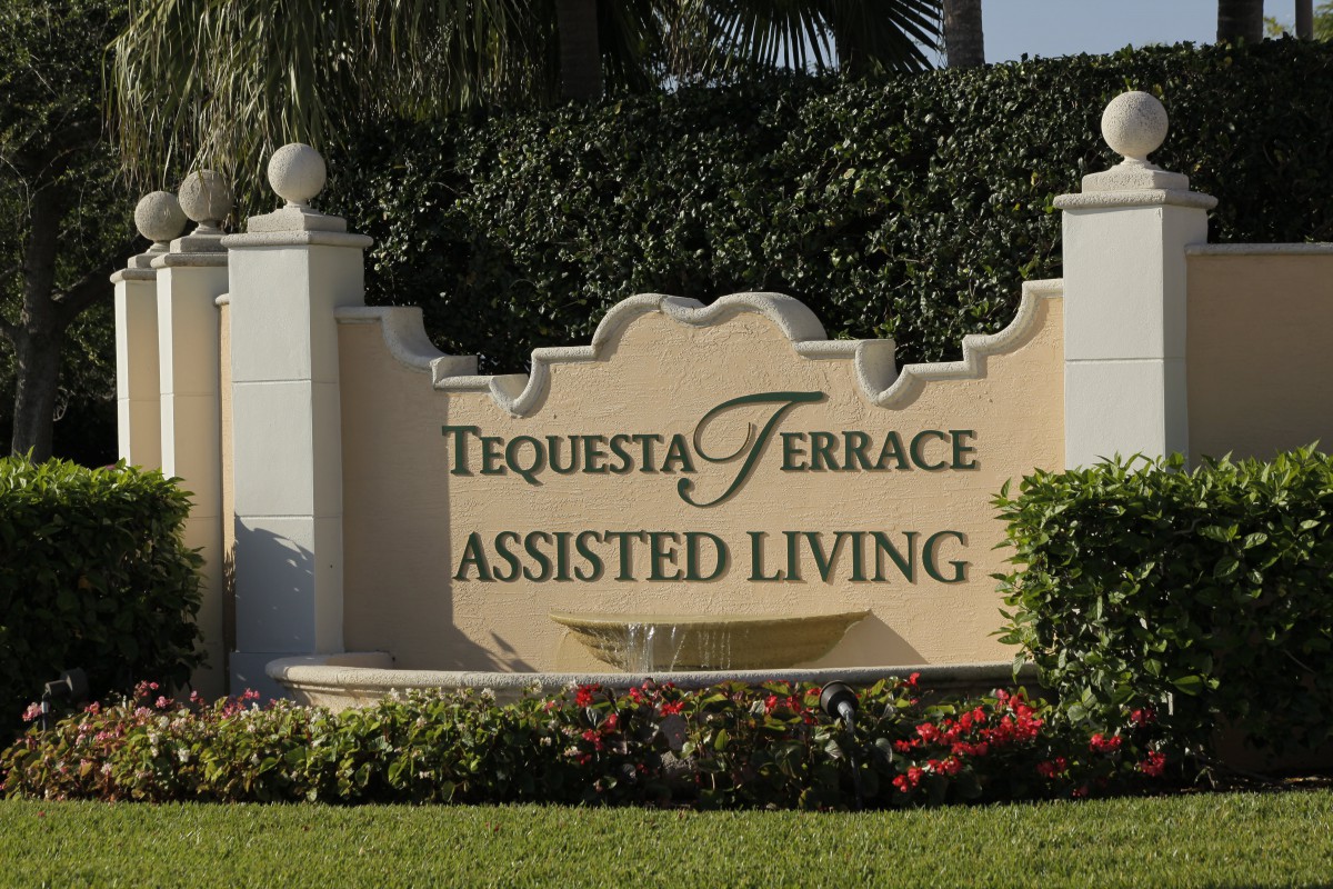 Sign for Tequesta Terrace Assisted Living surrounded by greenery and flowers.