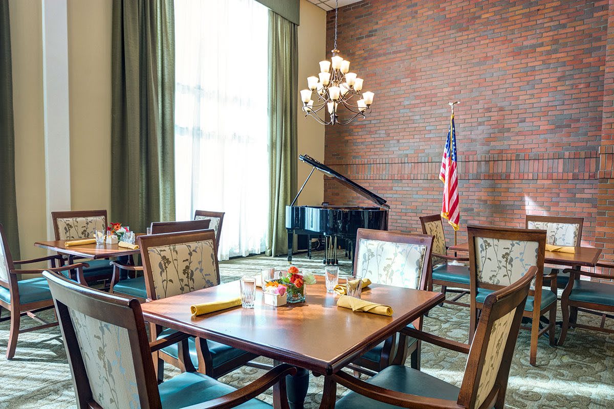 A cozy dining area featuring a piano and an American flag, with tables set for guests.
