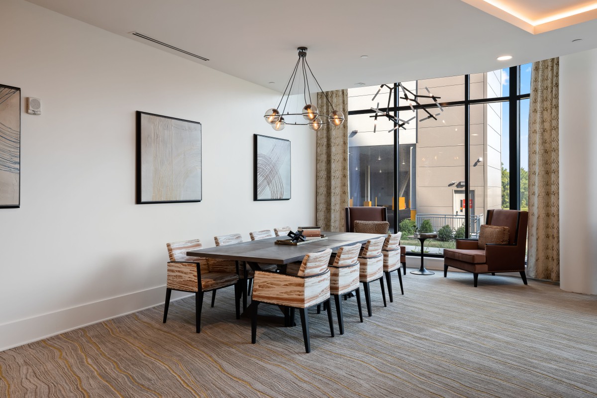 A modern dining room with a large table, wooden chairs, and stylish lighting fixtures.