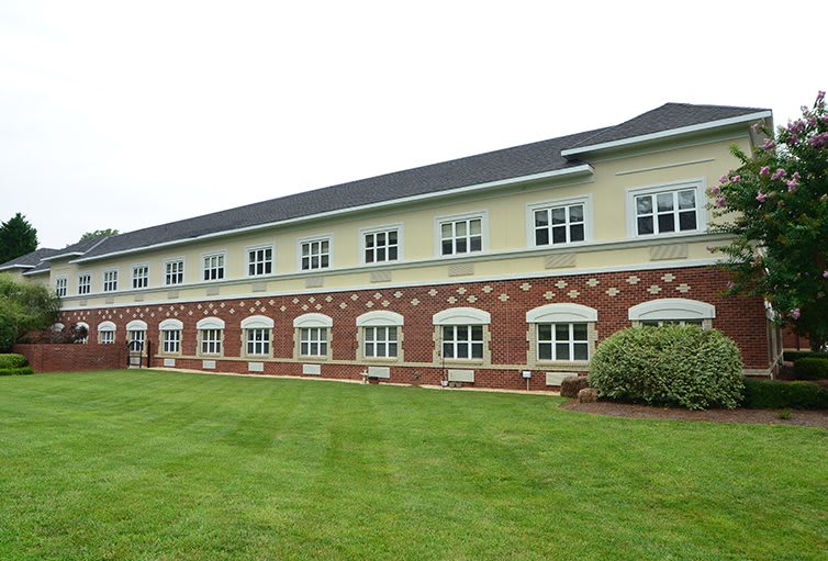 A two-story building with large windows and brickwork, surrounded by a well-maintained lawn.