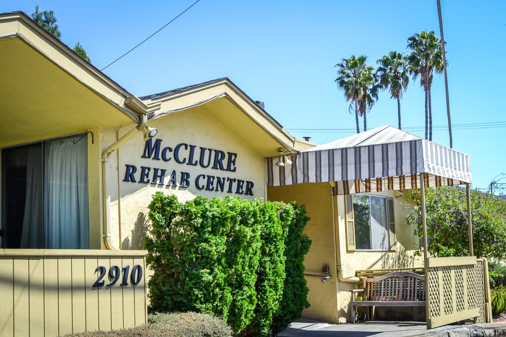 Exterior view of McClure Rehab Center with sign and surrounding greenery.