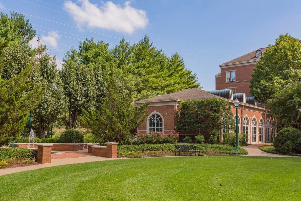 A brick building surrounded by lush trees and a well-maintained lawn on a sunny day.