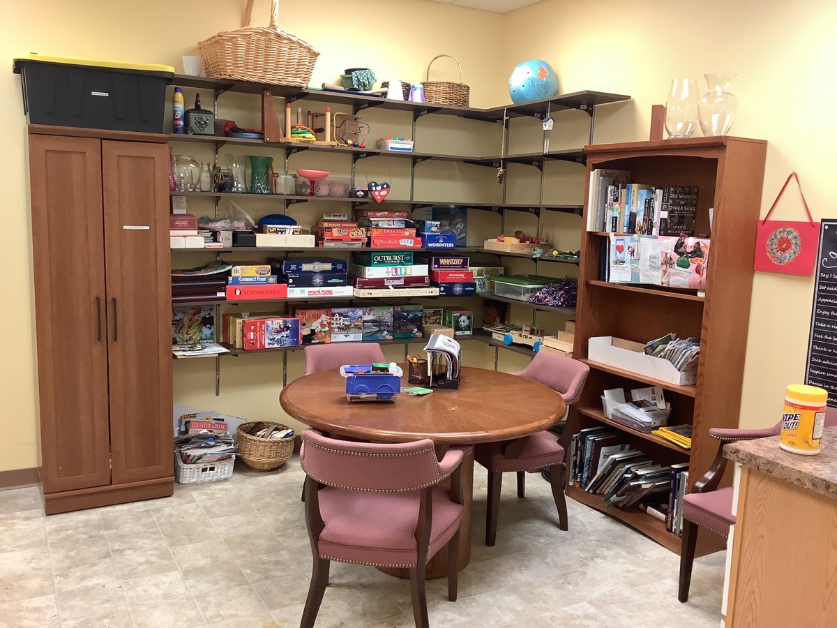 A cozy office space with a round table, chairs, and well-organized shelves filled with books and board games.