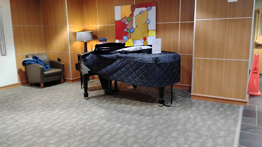 A grand piano covered with a protective quilt, set in a cozy interior space featuring modern artwork and a lamp.