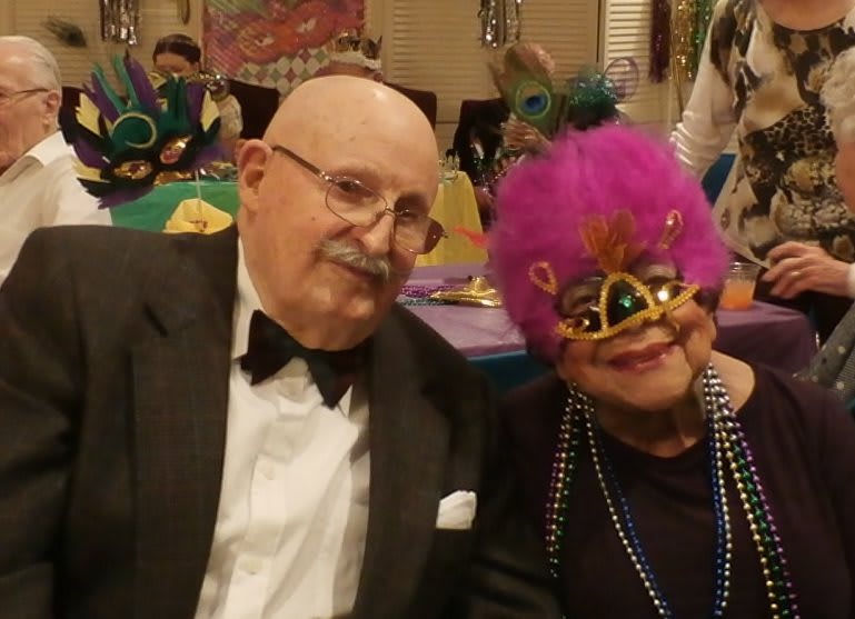 A couple enjoying a masquerade party, both dressed in formal attire with colorful masks.