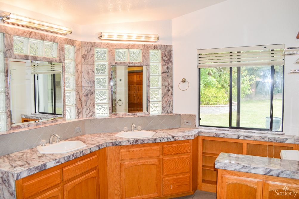 A spacious bathroom with marble countertops, dual sinks, wood cabinets, and large mirrors.