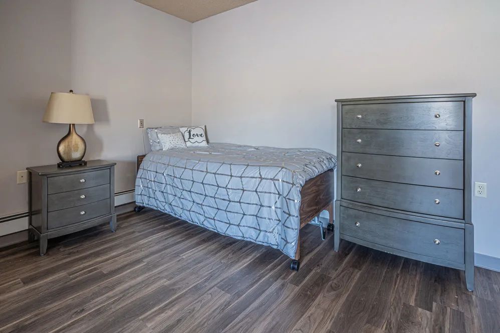A minimalist bedroom with a single bed, dresser, and nightstand.