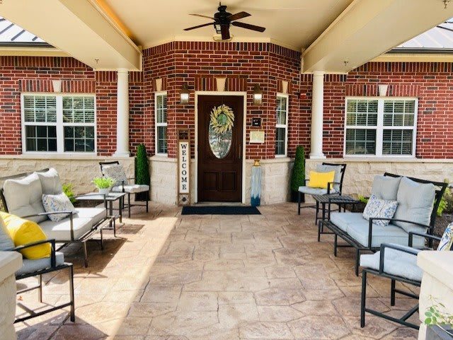 A welcoming porch with comfortable seating and a ceiling fan, framed by brick walls and columns.