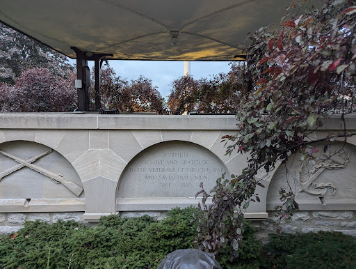 A serene monument surrounded by greenery and trees, partially sheltered under a canopy.