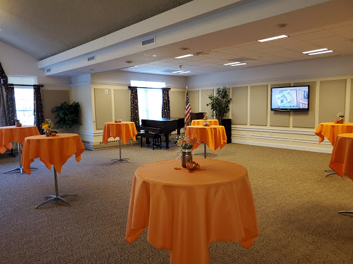 A spacious event room set up with orange tablecloths and a piano, ready for gatherings.