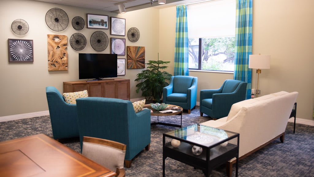 A cozy living room featuring blue armchairs, a television, and stylish wall decor.