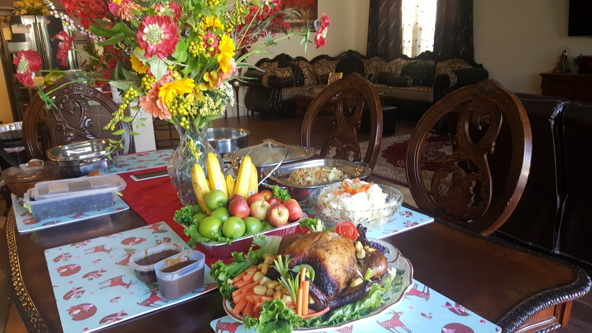 A beautifully set dining table with roast chicken and fresh fruits, accompanied by a vibrant flower arrangement.
