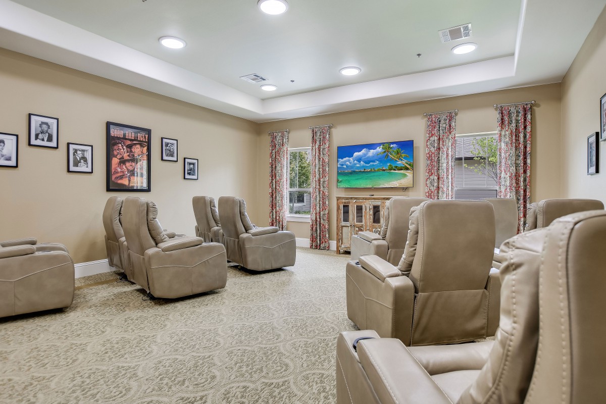 A cozy living room with recliner chairs facing a television, adorned with wall decor and curtains.