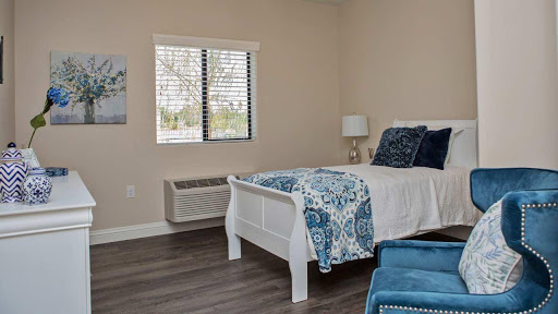 A cozy and modern bedroom featuring a white bed with blue accents, a window with blinds, and stylish furniture.