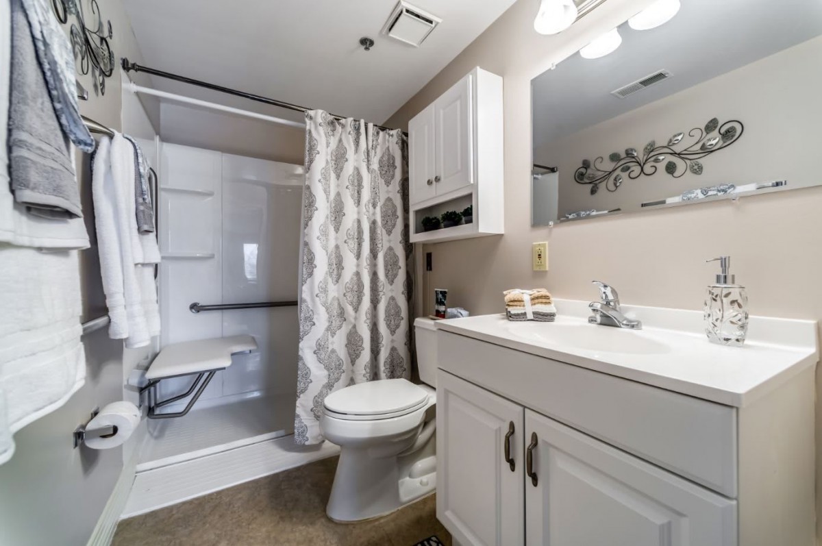 A well-organized bathroom featuring a shower with a curtain, toilet, sink with cabinets, and a mirror.